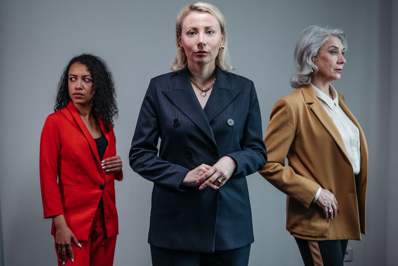 hero-img-02 Three businesswomen in suits pose confidently on a neutral background, showcasing diversity.